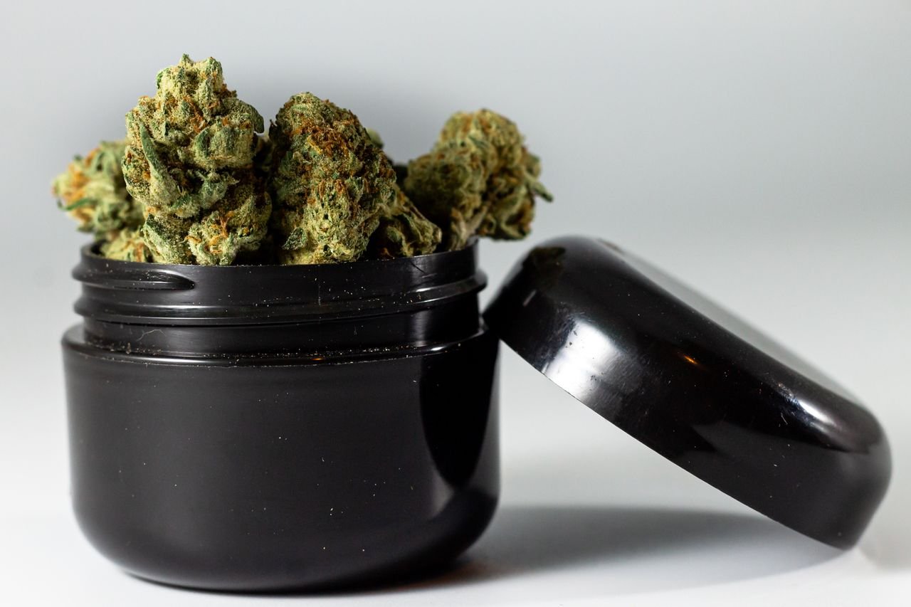 Services Detailed image of cannabis buds overflowing from a black jar, showcasing texture and color.
